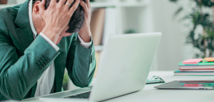 Stressed man holding head at desk with laptop.