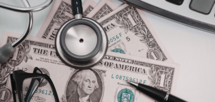 Medical costs with stethoscope, calculator, and dollar bills on a desk.