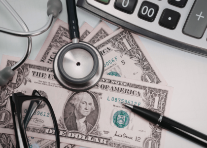 Medical costs with stethoscope, calculator, and dollar bills on a desk.
