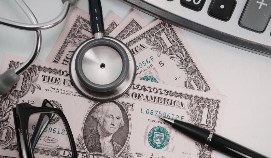 Medical costs with stethoscope, calculator, and dollar bills on a desk.